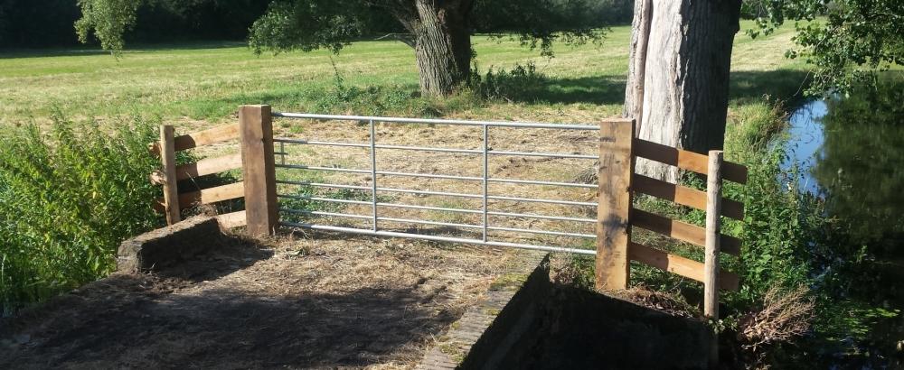 Houten toegangspoort met stalen hekwerk - ingang natuurgebied met water en boom